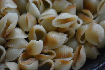 Food, cooking in a home kitchen. Boiled vermicelli, shaped like brown, black, yellow shells lies in an old, thick frying pan.