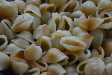 Food, cooking in a home kitchen. Boiled vermicelli, shaped like brown, black, yellow shells lies in an old, thick frying pan.