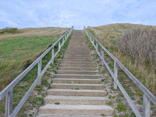 Stairs leading up to a grassy hill under a cloudy sky at a coastal location