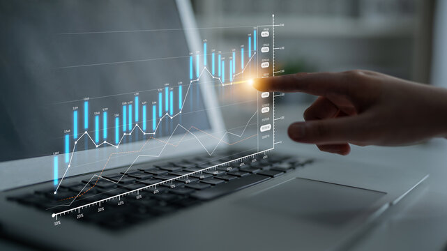A hand gestures towards a digital financial chart displayed on a laptop, symbolizing investment growth and modern technology in analysis and business strategy. Scalp