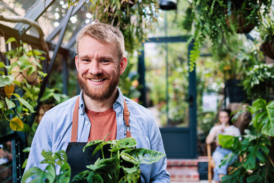 Happy greenhouse owner with blond hair wearing apron