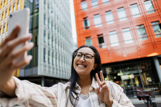 Smiling woman taking selfie with peace sign in urban city outdoors