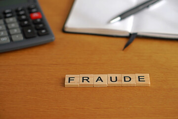 fraude. conceptos financieros. palabra escrita en con letras de madera con calculadora libreta y boligrafo al fondo