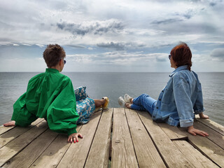 Two friends enjoying a calm day by the water on a wooden pier overlooking the serene ocean view
