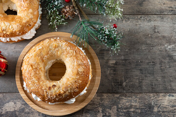 traditional Spanish Roscón de Reyes filled with whipped cream, decorated with sliced almonds and sugar on top on wooden table. Top view. Copy space