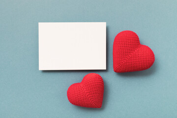 Knitted red hearts and clean paper blank on blue background for Valentine day greeting card.