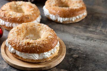 traditional Spanish Roscón de Reyes filled with whipped cream, decorated with sliced almonds and sugar on top on wooden table. Copy space