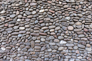 A full frame texture background of a rustic wall made of round, smooth stones