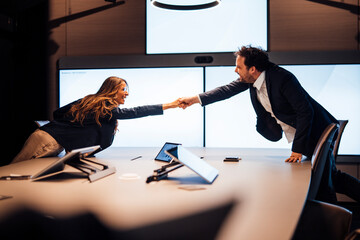 Business professionals shaking hands over meeting table in modern office
