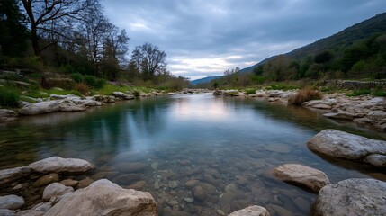 Clear river flowing through a rocky forested landscape under a cloudy sky at dusk