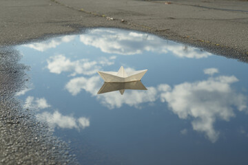 delicate paper boat floats in puddle perfectly reflecting sky above