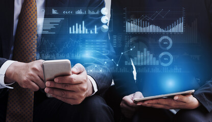 Two business professionals sit together engaged with their devices while reviewing digital financial data and visualizations in a contemporary office setting. Scalp