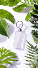 A blank rectangular keychain with a metallic loop is centrally placed, framed by various green leaves and tropical foliage on a white surface.