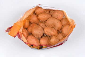 A studio photograph captures a mesh bag of fresh red potatoes lying on a light gray background, highlighting the contrast between the rough skin and the fine net