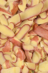 A close-up, full-frame photograph shows a pile of raw potato peelings with red skin and yellow flesh, creating an organic, overlapping texture