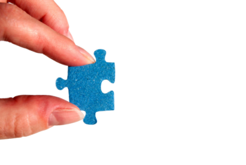 A hand holding a puzzle piece. Fingers with a blue jigsaw puzzle piece close-up.