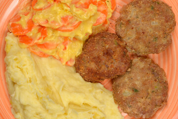 A close-up, top-down view shows three browned meat patties, creamy mashed potatoes, and carrots in a light sauce on a peach-colored plate