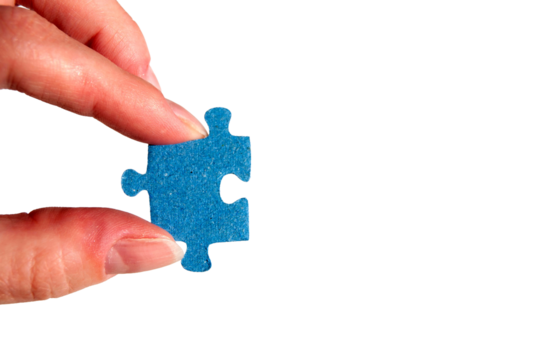 A hand holding a puzzle piece. Fingers with a blue jigsaw puzzle piece close-up.