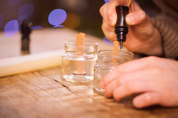 Hands of a person carefully pouring wax into small glass jars with wooden wicks, creating homemade candles, showcasing the art of candle making and craftsmanship in a cozy environment