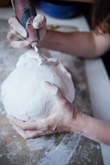 Skilled artisan shaping a clay sculpture with a rotary tool, showcasing intricate details and craftsmanship in a creative workspace filled with materials and tools