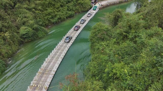 Aerial drone shot of the Shiziguan floating bridge in Hubei, China, showing cars crossing over green river water surrounded by dense forest and mountains.