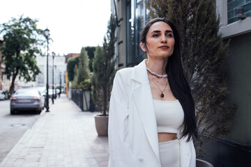 Confident woman in stylish white outfit stands on urban street, showcasing modern fashion sense and self-assured demeanor in a vibrant city environment