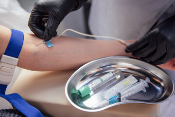 Medical professional in black gloves prepares to draw blood from a patients arm, showcasing medical tools and a sterile environment for healthcare procedures