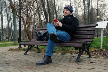 Young man relaxing on park bench and listening to music with headphones