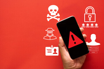 Cybersecurity threat concept. Hand holds a smartphone with a warning alert, symbolizing a data breach, phishing attack, virus, and hacker stealing passwords and personal identity on a red background.