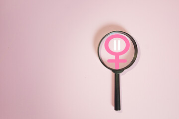 Menopause and women's health concept. Magnifying glass focusing on a female gender symbol with a pause icon, symbolizing aging, hormonal changes,medical research,and examination on a pink background.