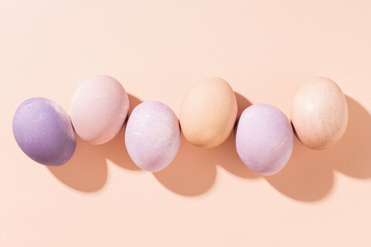 Row of pastel colored Easter eggs on peach background, top view, hard light.