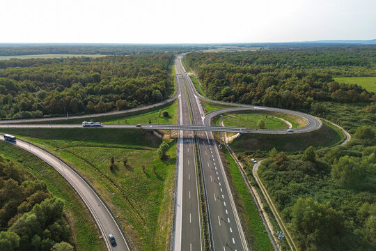 Aerial view of a modern highway interchange cuts through a vibrant green forest, a stark contrast of human engineering and natural beauty, Zagreb, Croatia.