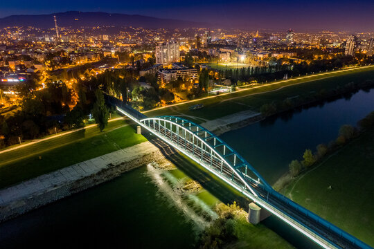 Aerial view of the illuminated arches of Domovinski Most bridge reflecting in the calm Sava River under a star-dusted sky, Zagreb, Croatia.