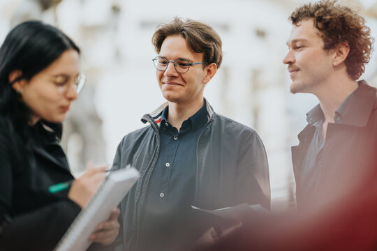 Three professionals converse outside, taking notes and sharing documents. A relaxed, collaborative moment in an urban setting, reflecting teamwork, communication, and positive energy.