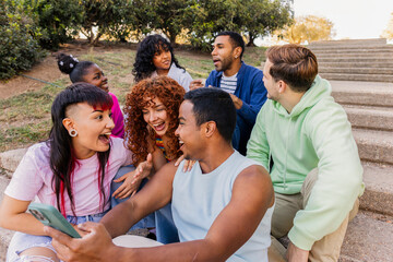 Diverse friends laughing and sharing phone outdoors