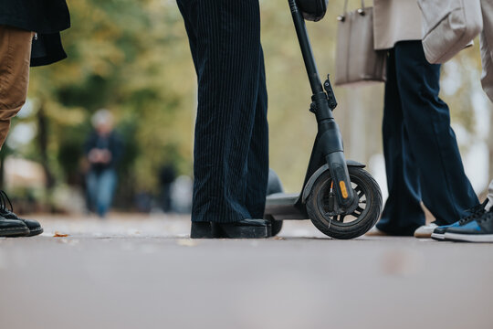 A group of professionals stand near an electric scooter on a city path, dressed in smart casual and suits. The scene conveys urban connectivity, everyday commute, and informal collaboration outdoors.