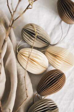 Easter paper eggs pastel colored decorations, made out of cardboard and branches on linen tablecloth.