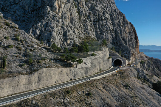 Aerial view of a road disappearing into the dark mouth of a tunnel carved into the stark, rocky mountainside, Split-Dalmatia County, Croatia.