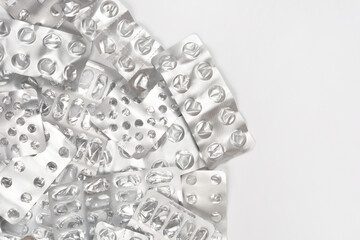 A horizontal shot of a pile of empty, crumpled silver medicine blister packs filling the bottom half of the frame against a white background with copy space above