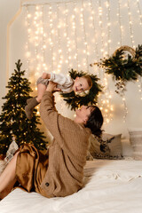 Mother hugs her baby boy above her in a festive Christmas room and he is happy