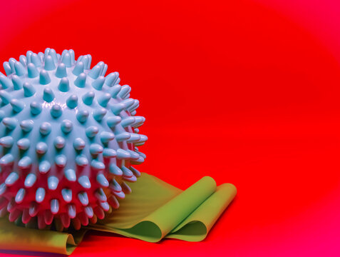 Blue spiky massage ball and rolled green resistance band on bright red background. Minimal fitness composition with physiotherapy and rehabilitation concept. Sport recovery and home workout equipment.