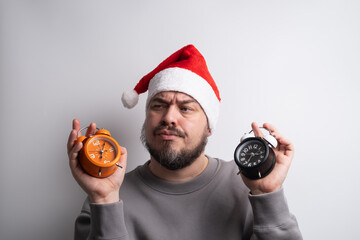 Confused man in santa hat holding two alarm clocks