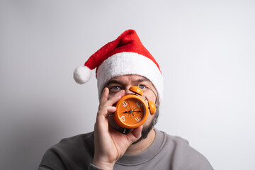 Confused man in santa hat holding two alarm clocks