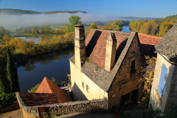 Traditional medieval houses with sloping slate roofs in the village Beynac et Cazenac, Dordogne, France, blend into a magnificent cliff and overlooking the river Dordogne, with autumn morning mist