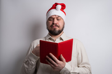 Man in santa hat reading red notebook for list confirmation and planning. Holiday review.