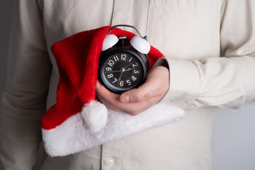 Hand holding alarm clock wrapped in santa hat