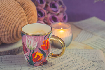 Warm latte in floral cup with candlelight and knitted textures, cozy autumn mood