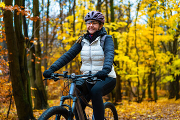 Beautiful middle-aged woman riding bicycle in forest in autumn. Front view	