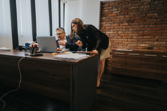 Two coworkers are reviewing information on a laptop in a professional office environment. - Powered by Adobe
