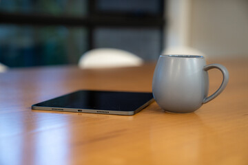 Grey mug and tablet on wooden table in indoor workspace